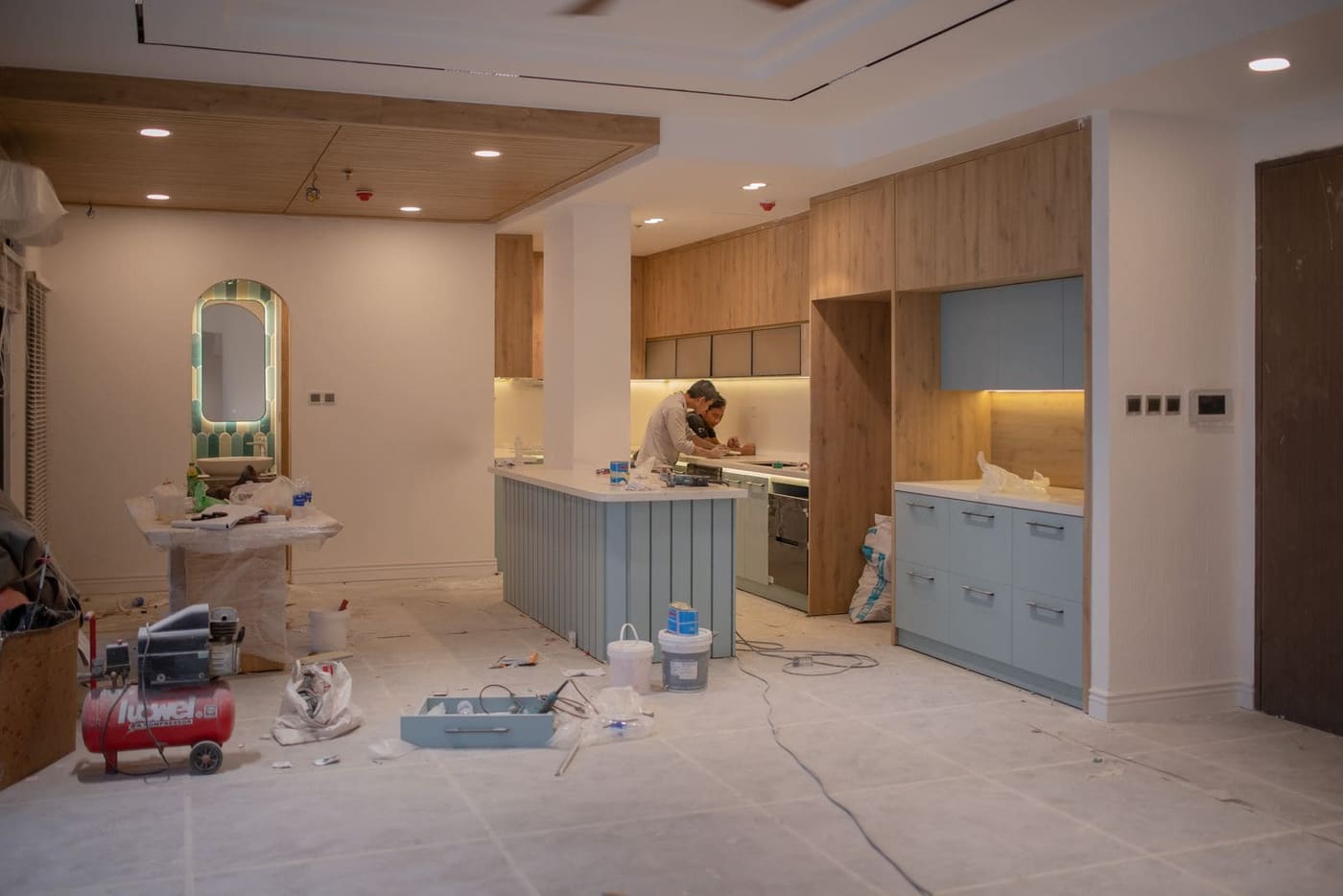 A kitchen part way through a renovation, with timber cabinets in and a tradesman at the bench