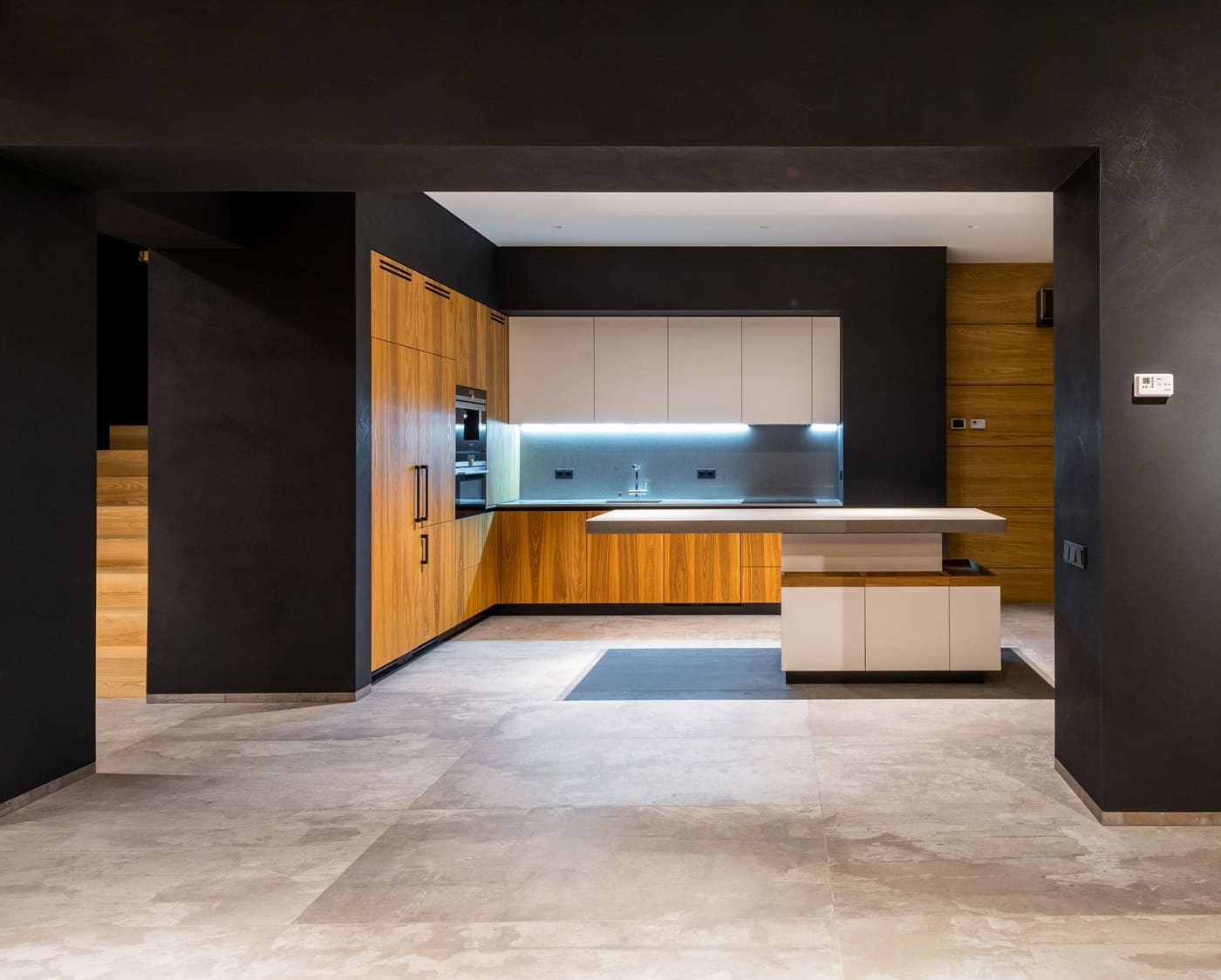 A finished kitchen with timber cabinets, a white island bench and charcoal walls