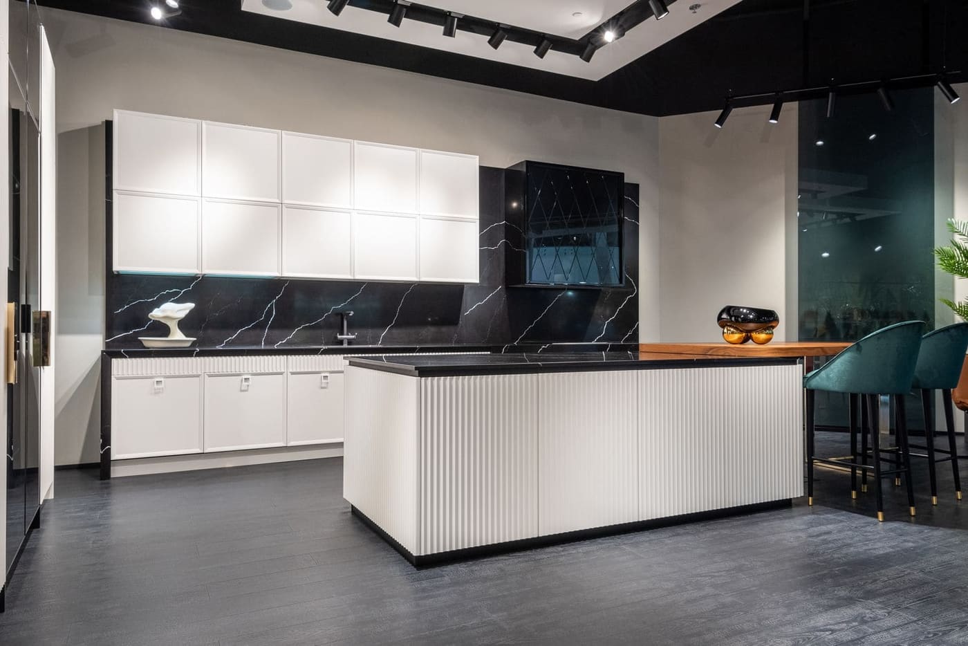 A white kitchen with a ribbed island bench and a black stone splashback