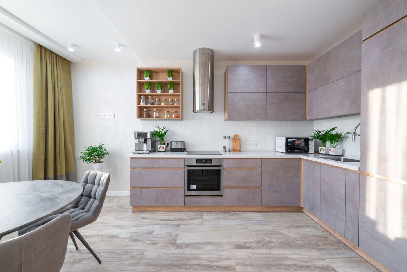 A kitchen with grey cabinets, open timber shelves and a round dining table