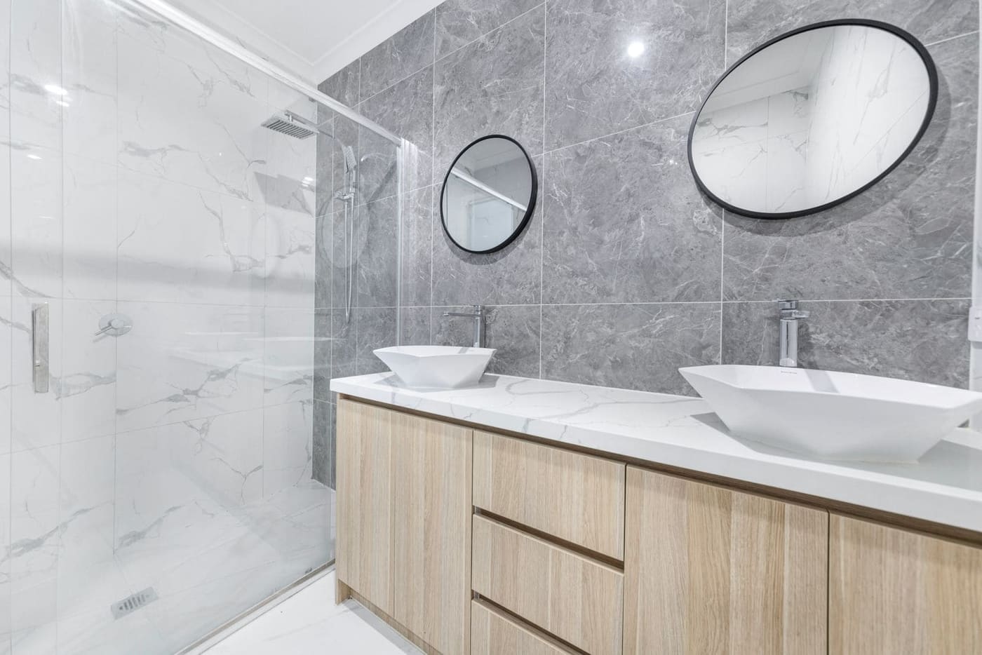 A bathroom with two basins on a timber vanity and grey marble-look tiles
