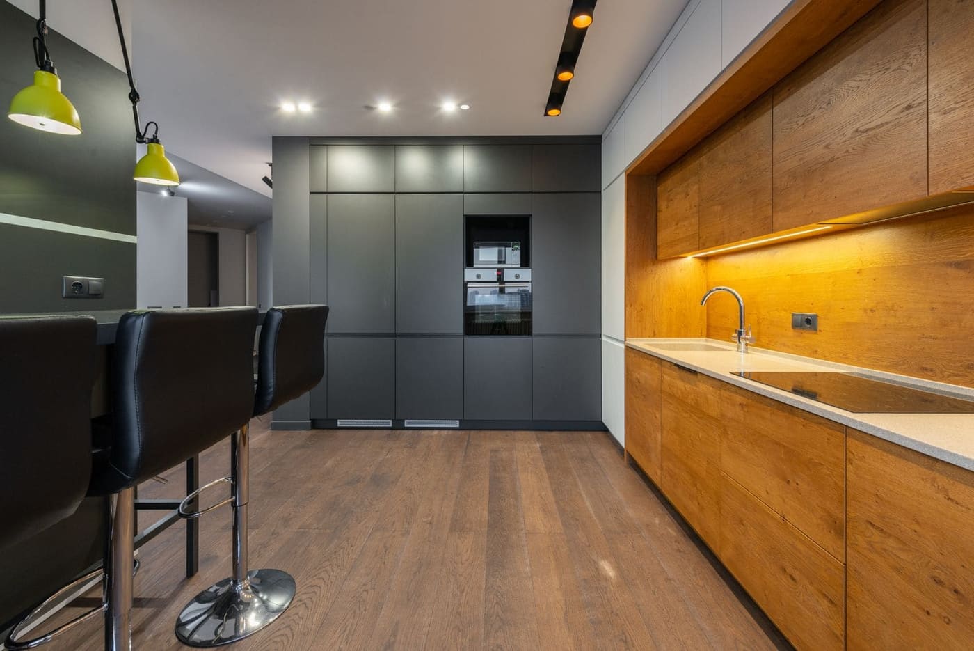 A long kitchen with timber cabinets, a charcoal wall of cupboards and bar stools