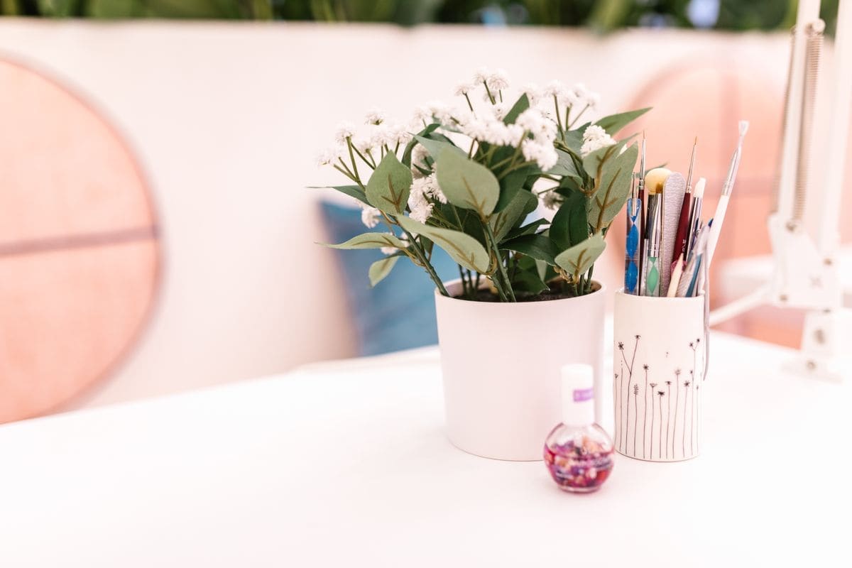 A white table with a pot of flowers and a cup of brushes