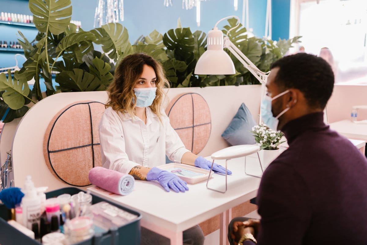 A technician at a pale pink manicure table with a client