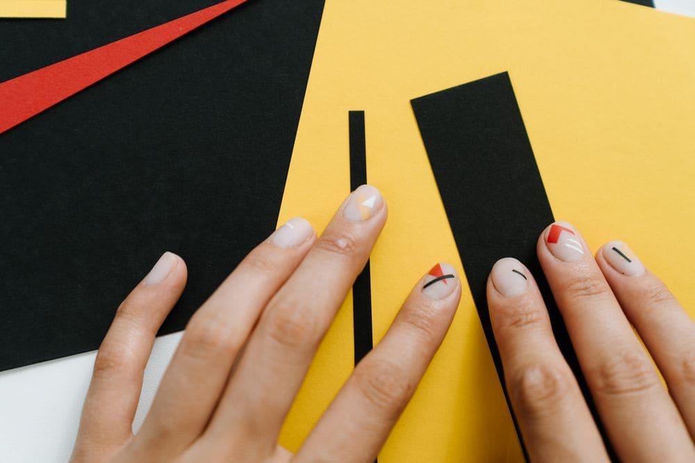 Hands with nude nails and thin painted lines against yellow and black paper