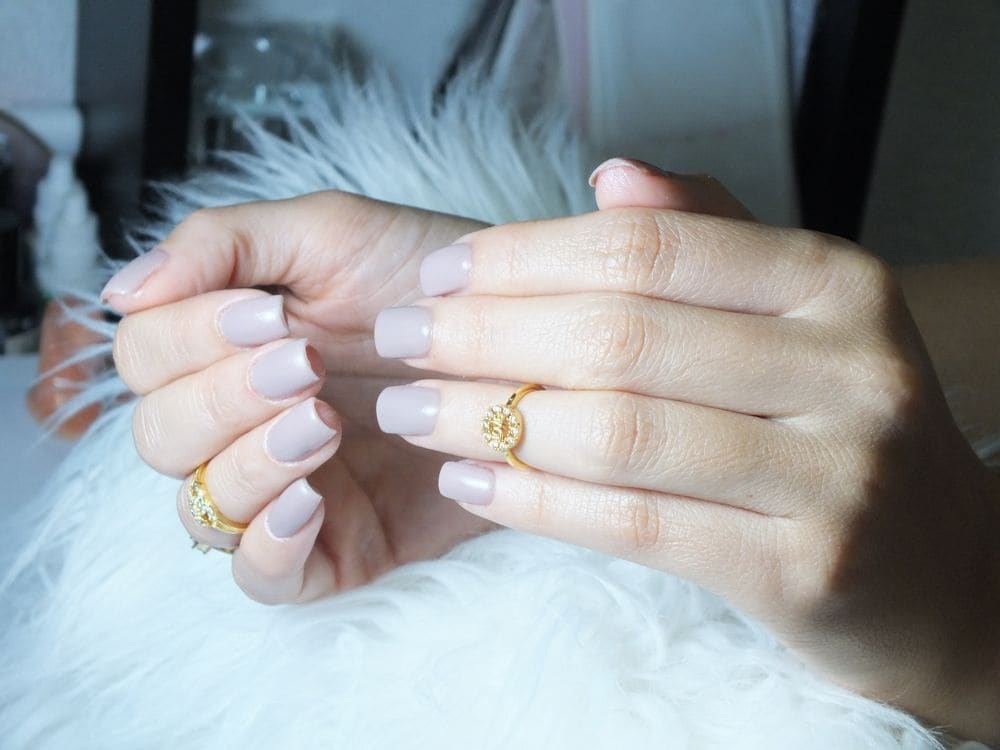 Hands with short, glossy nude nails resting on soft white fur