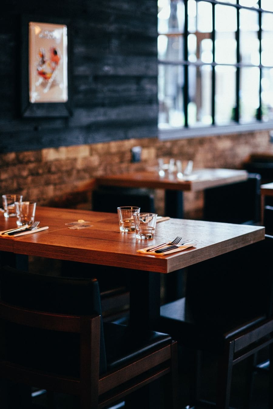 A timber table set with glasses by a brick wall