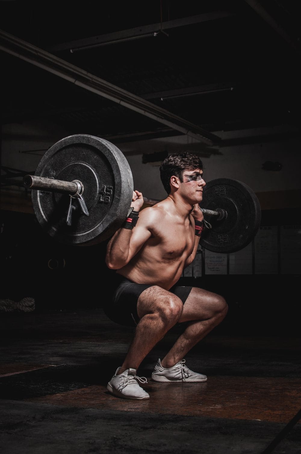 A man squatting a loaded barbell in a dark gym