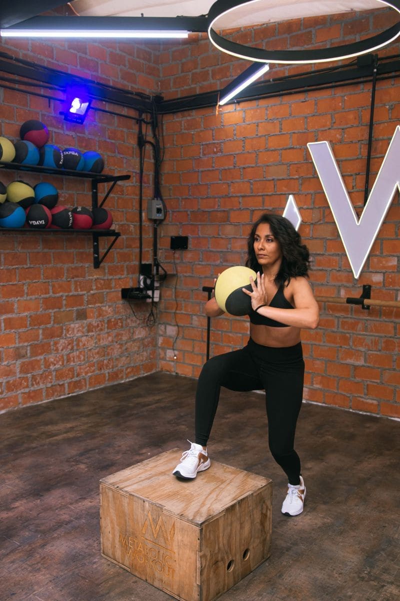 A coach holding a medicine ball by a brick wall