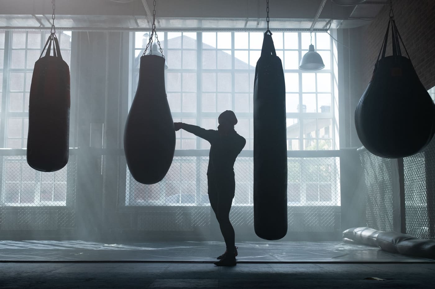 A boxer training on a heavy bag in a gym lit by tall windows