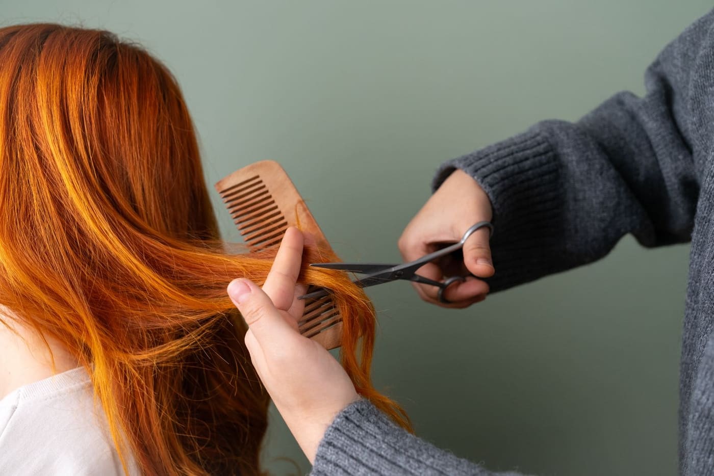 A stylist cutting long copper hair with a comb and scissors
