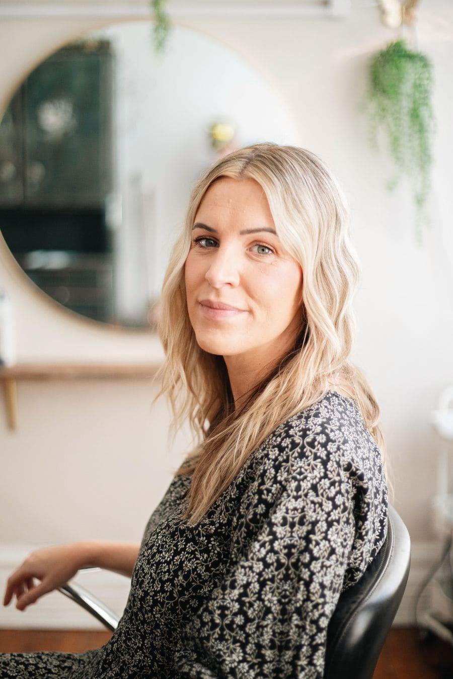 A smiling stylist with long blonde hair in a patterned dress