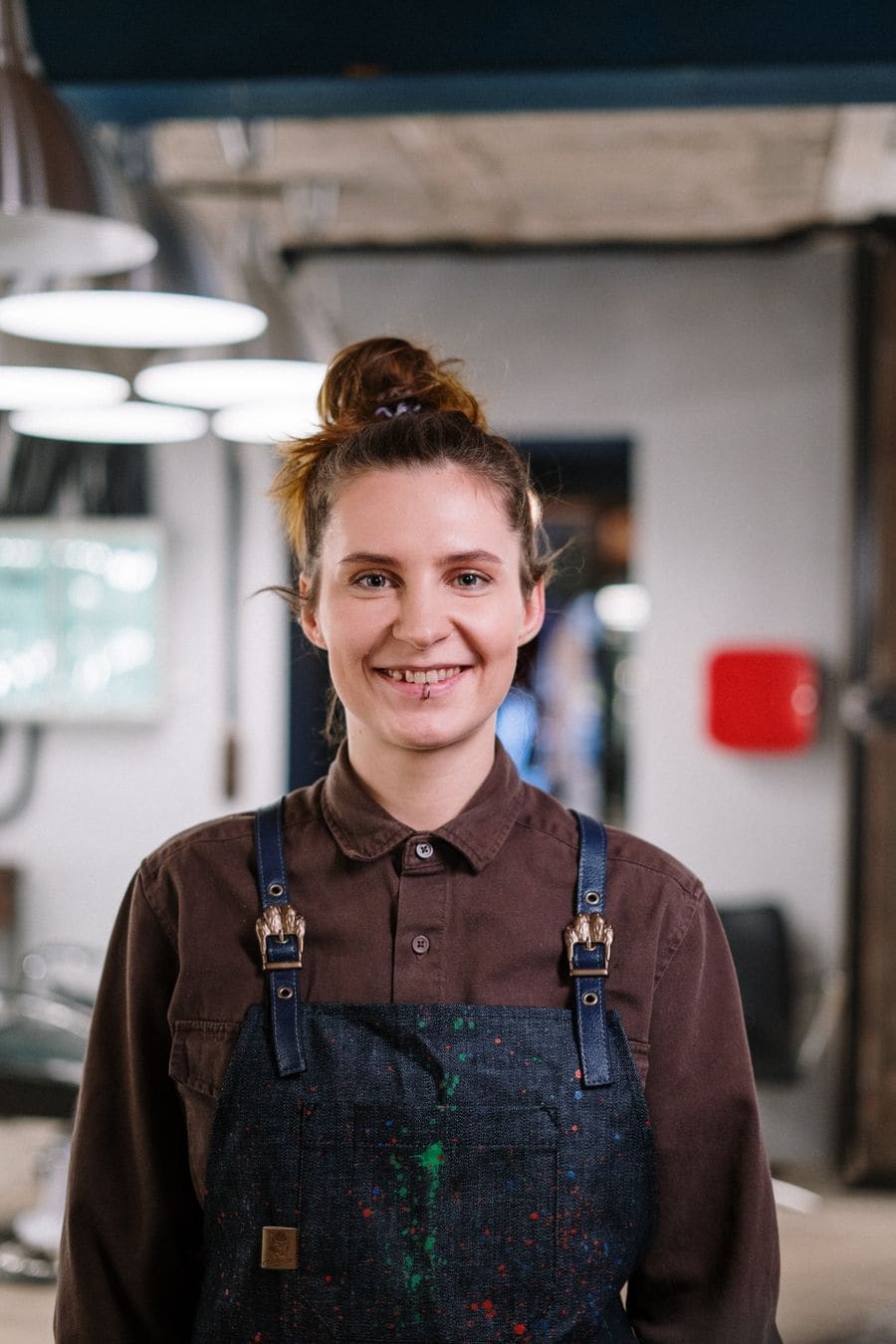 A smiling stylist with her hair tied back, in a brown apron