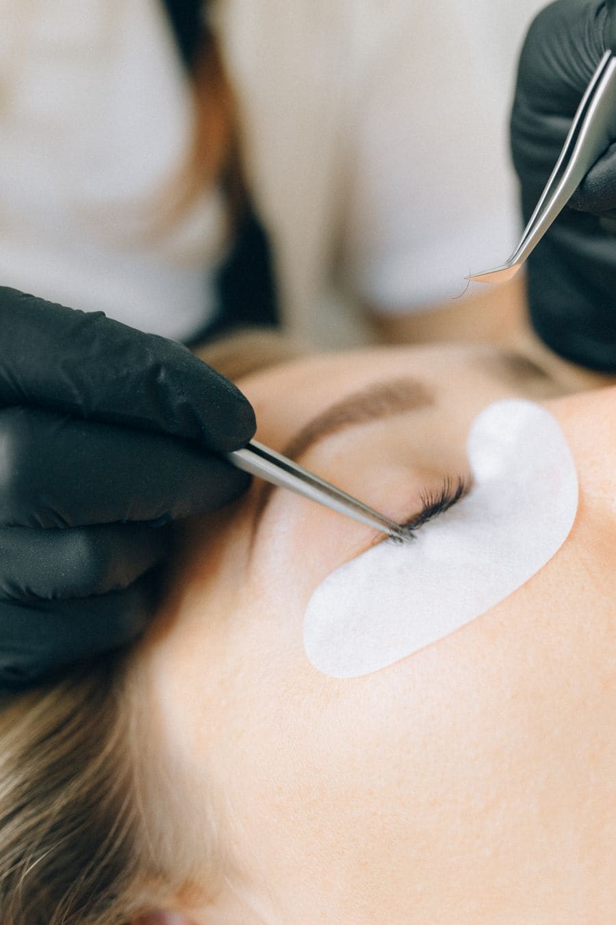A lash artist working with tweezers on a client's lashes