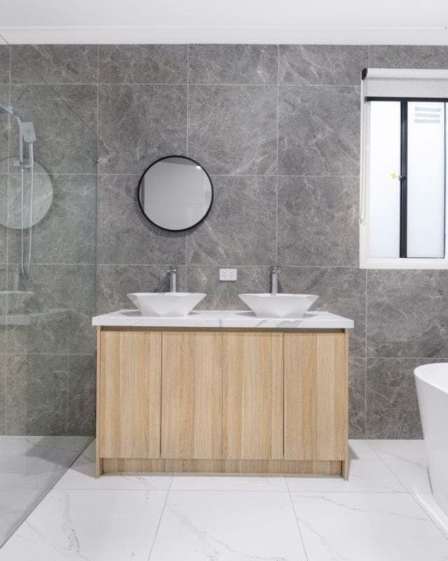 A grey and white bathroom with a freestanding bath, a timber vanity and two round basins