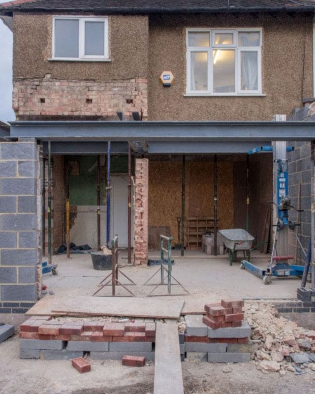 The brick back wall of a house opened up for a new extension, with steel posts in place