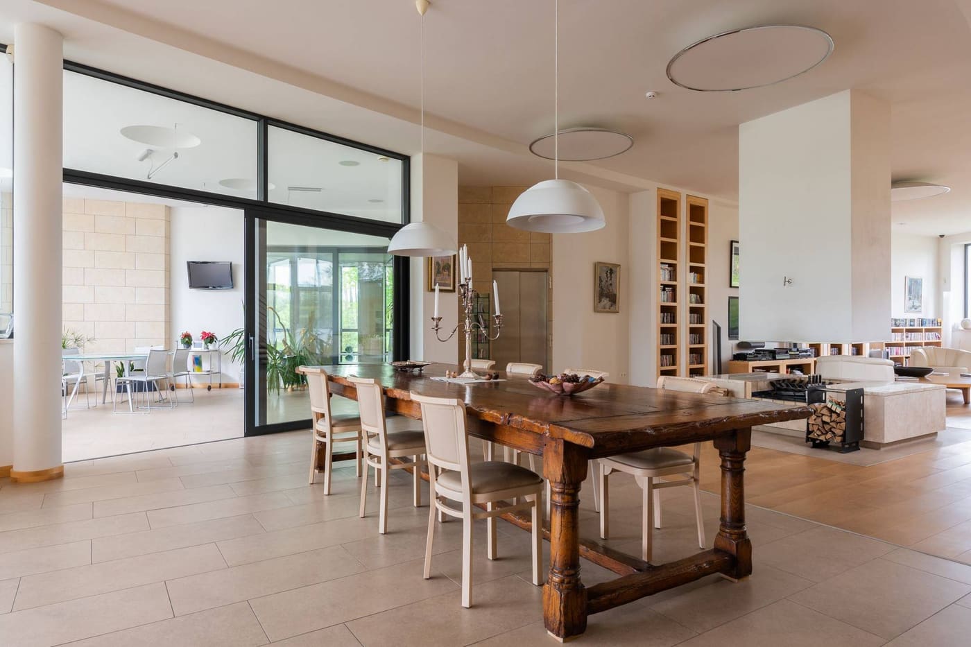 An open living and dining room with a long timber table, white walls and tall glass doors