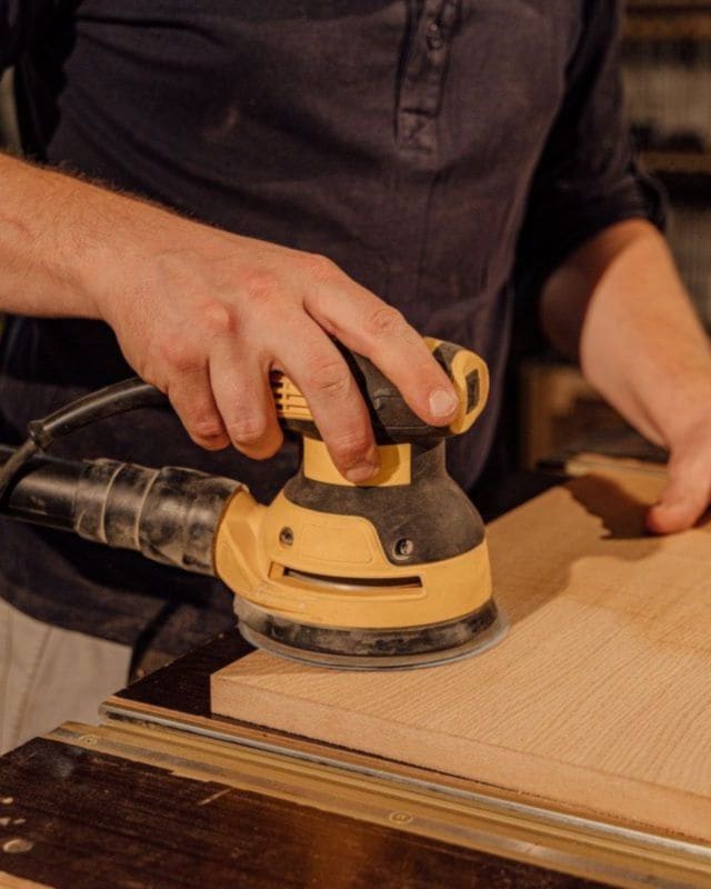 A joiner sanding a timber board in a workshop