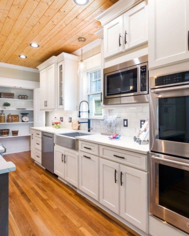 A white kitchen with timber floors, a long island bench and stainless steel ovens