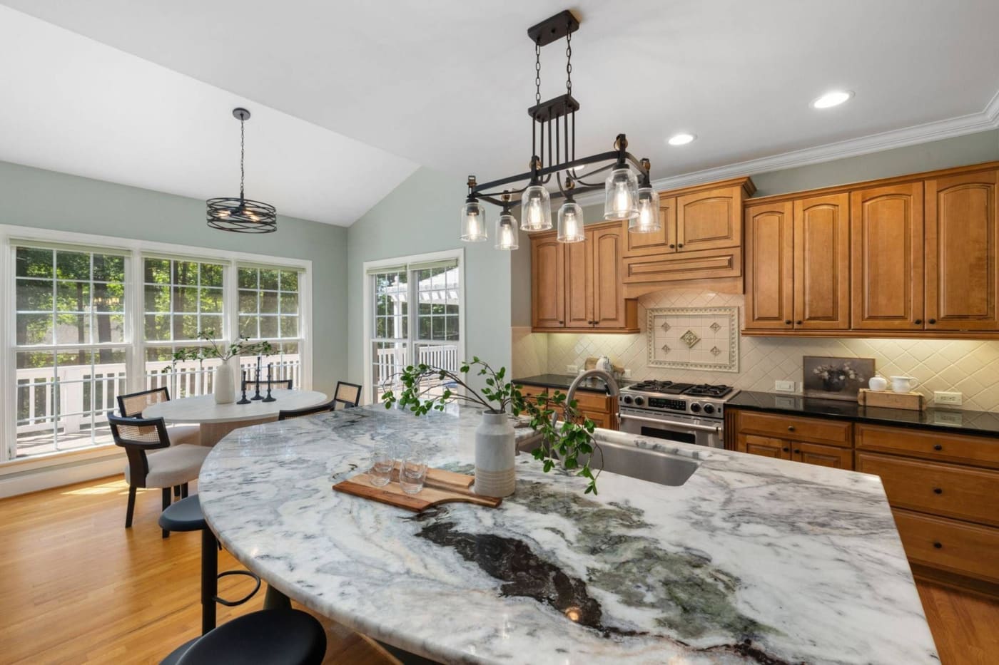 A renovated kitchen with a marble island bench, black pendant lights and timber floors