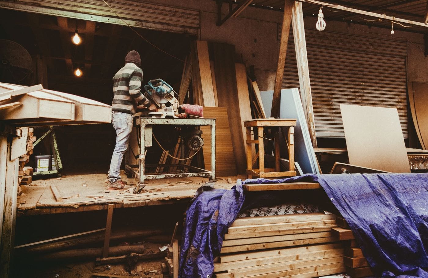 A builder cutting timber in a workshop lit by hanging bulbs