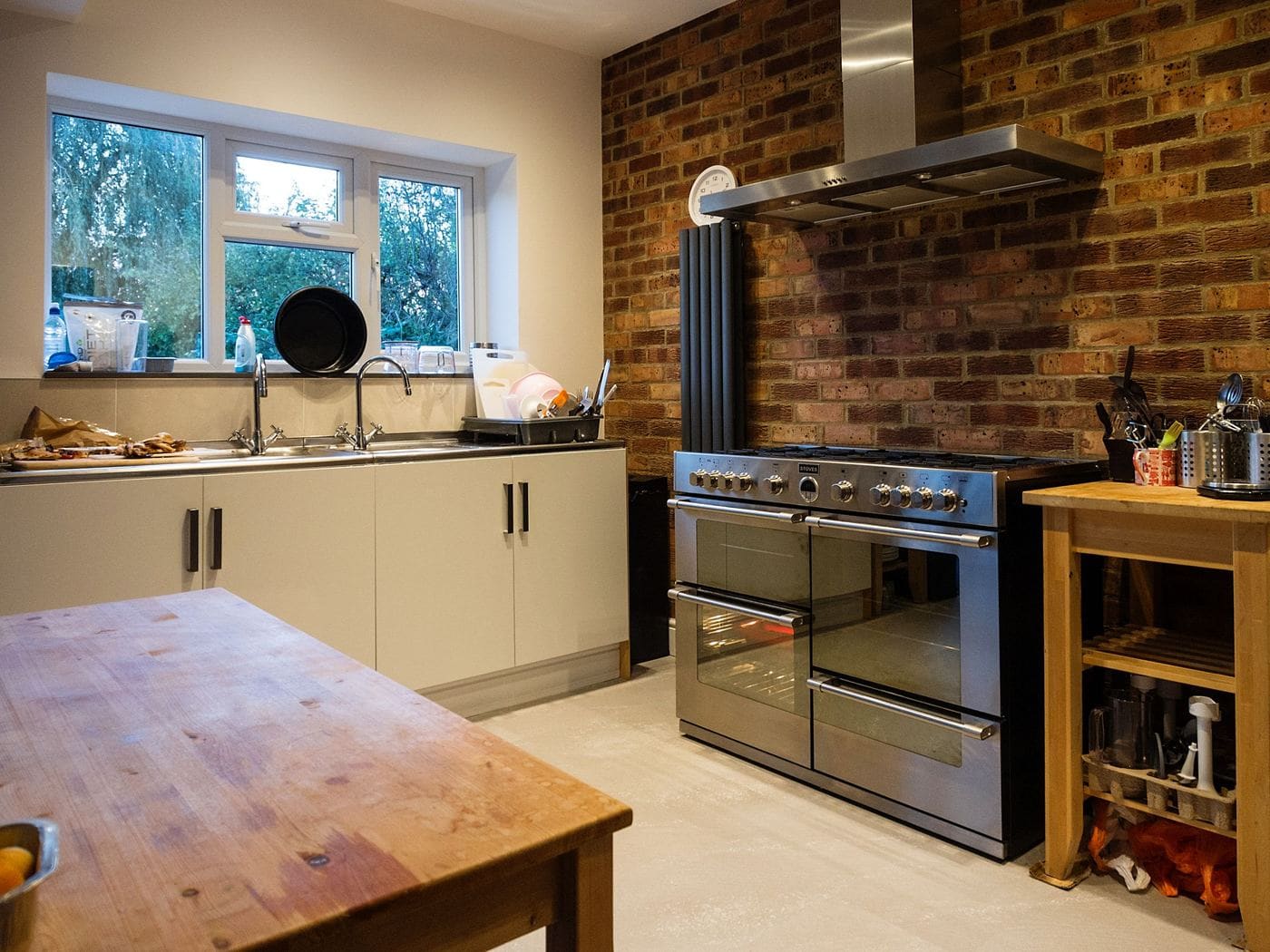 A kitchen with a brick wall, a black range hood and pale cabinets