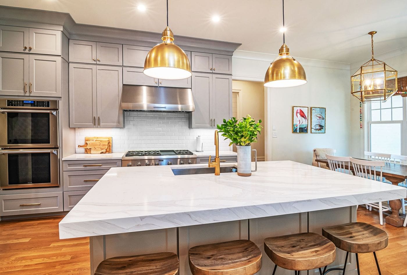 A white kitchen with a marble island, brass pendant lights and timber stools