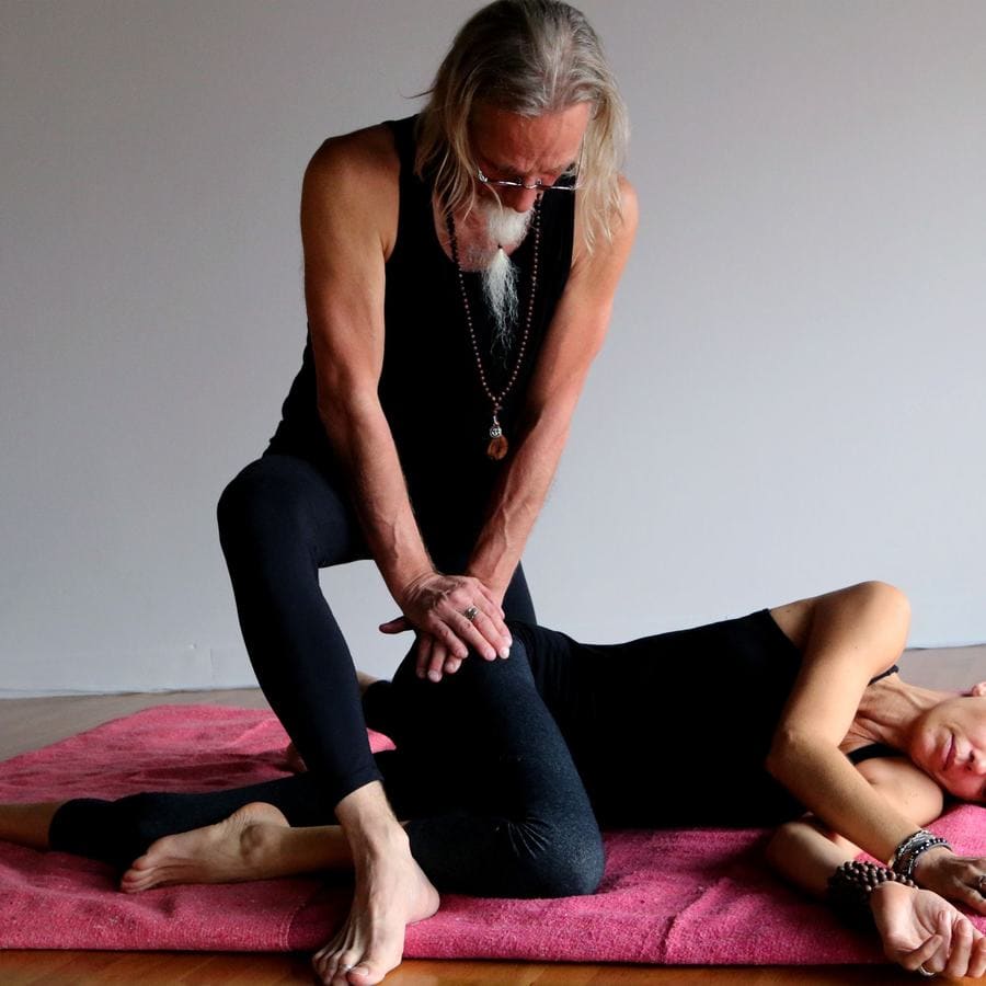 A teacher guiding a student through a stretch on a pink mat