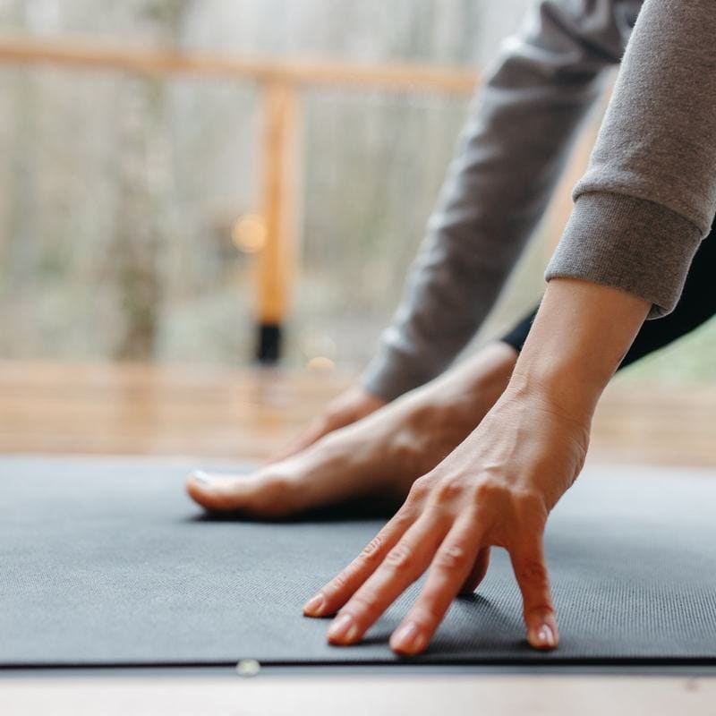 Hands and feet on a grey mat at the start of a forward fold