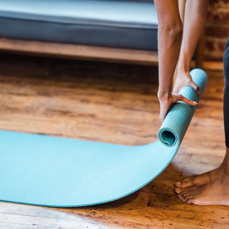 Hands rolling out a blue yoga mat on a timber floor