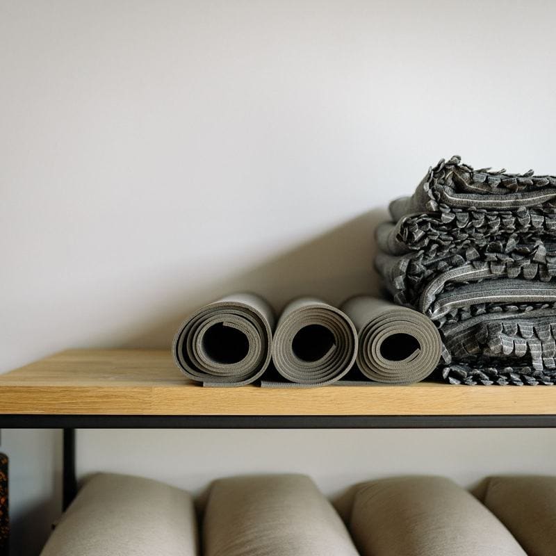 Rolled mats and folded blankets on a timber shelf above bolsters