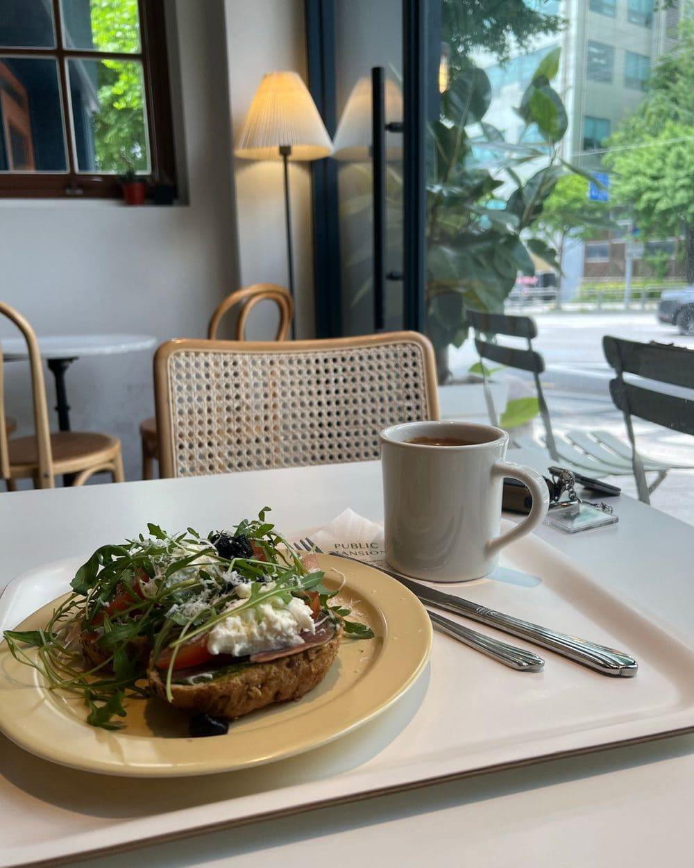 A plate of toast with greens beside a cup of coffee at a window table