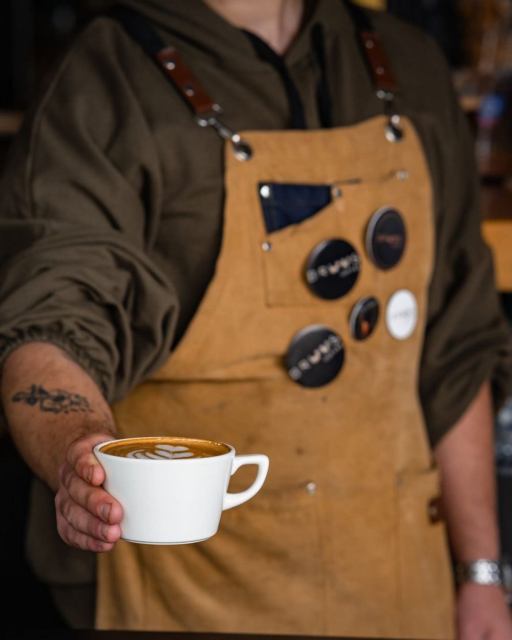 A barista in a canvas apron holding out a cup of coffee