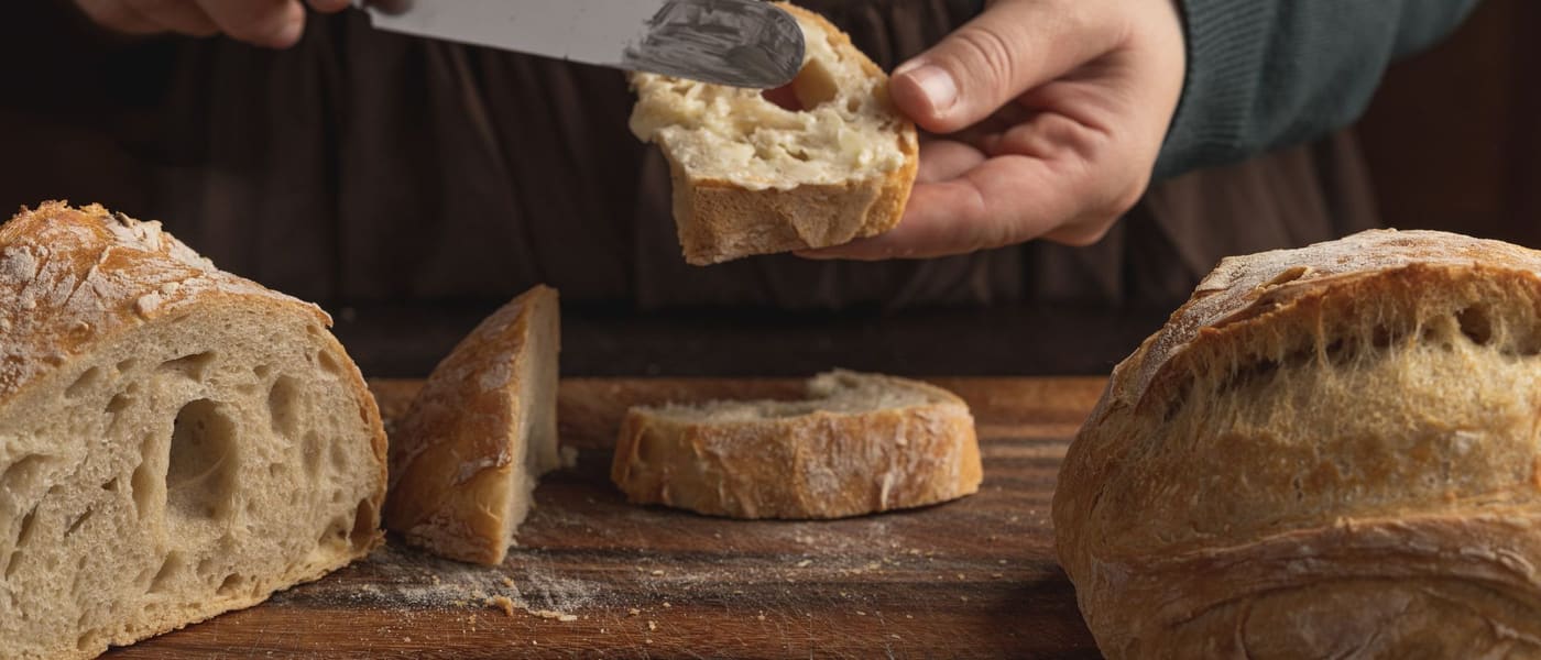 Hands buttering slices of sourdough beside whole loaves on a board