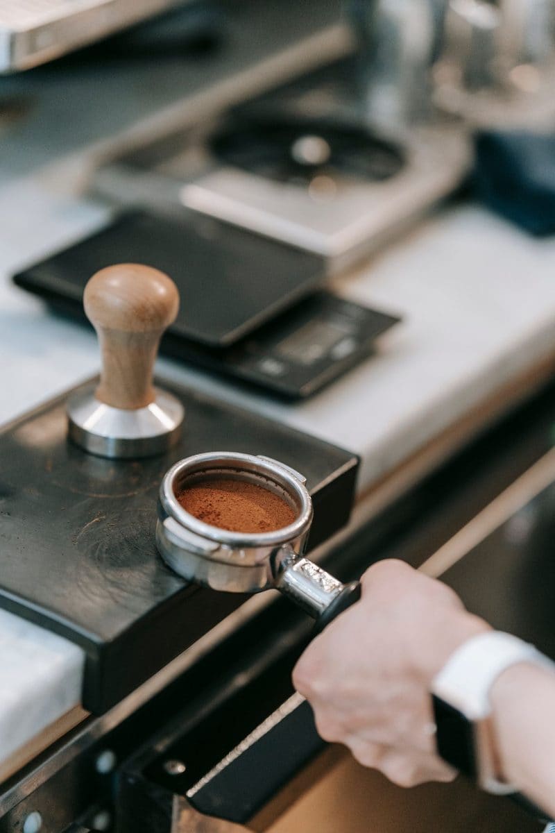 A hand tamping coffee into a portafilter beside the grinder