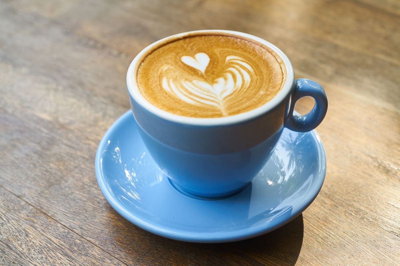 A flat white with a heart in the milk, in a blue cup on a timber table