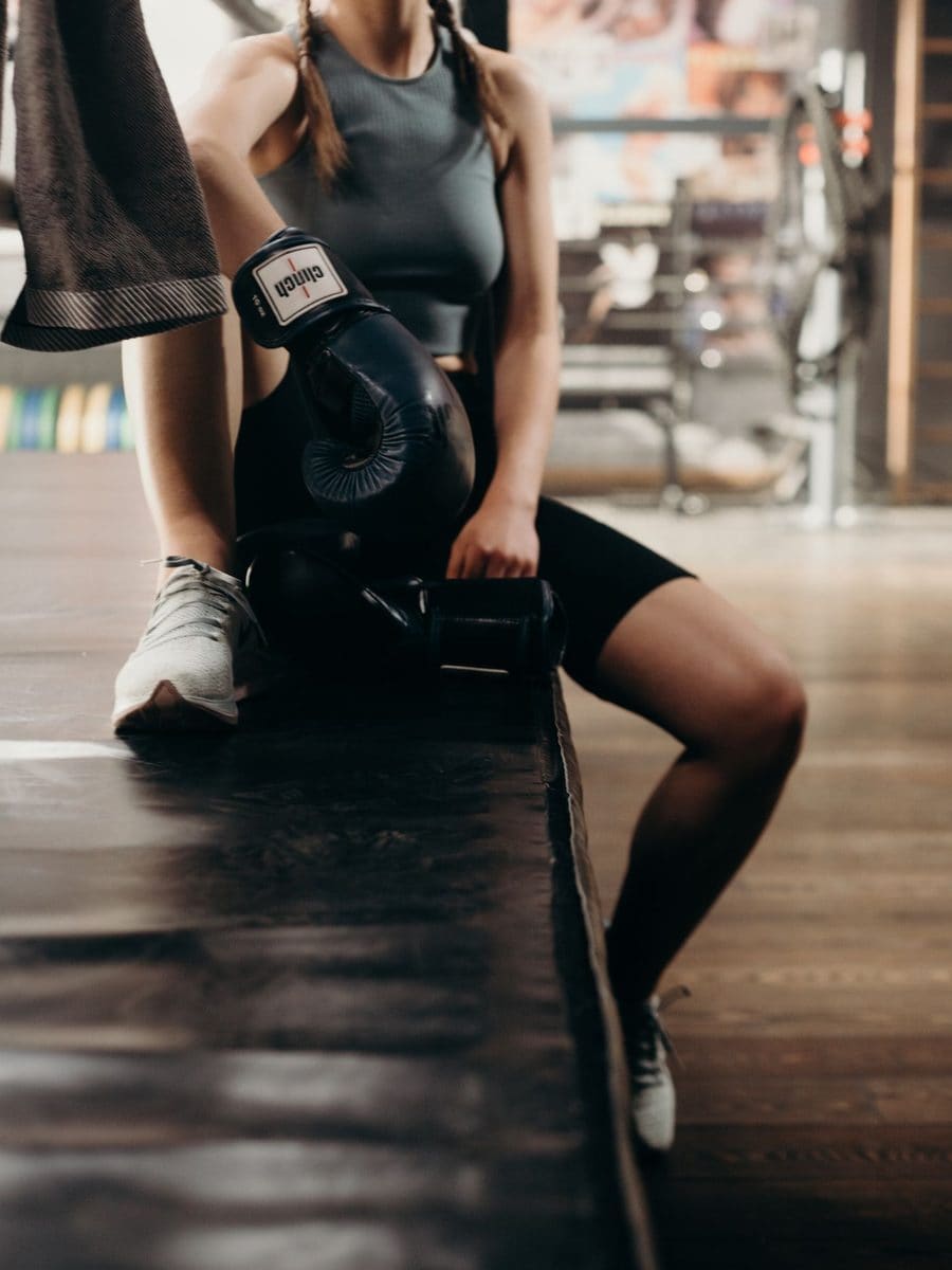 A woman in boxing gloves resting on a bench between rounds
