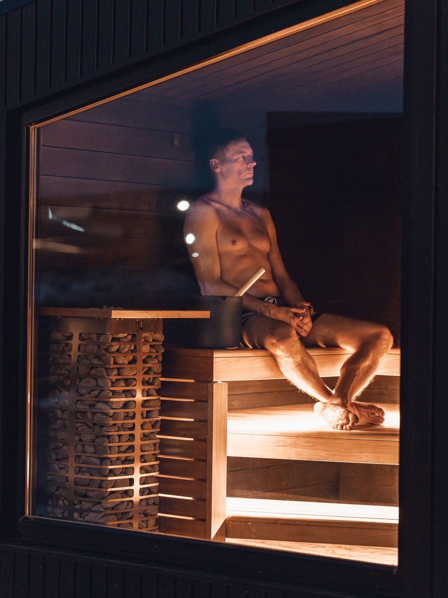 A man sitting in a timber sauna, seen through the glass