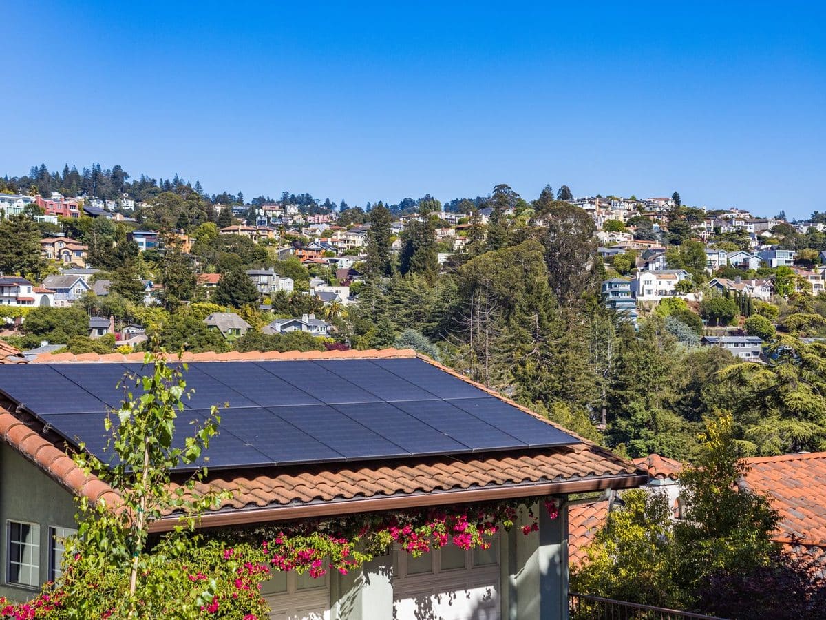 A house with a tiled roof covered in solar panels, with the town behind it