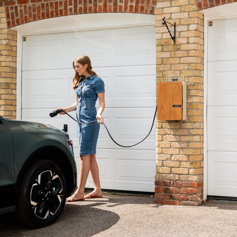A woman plugging a charging cable into an electric car in front of a garage