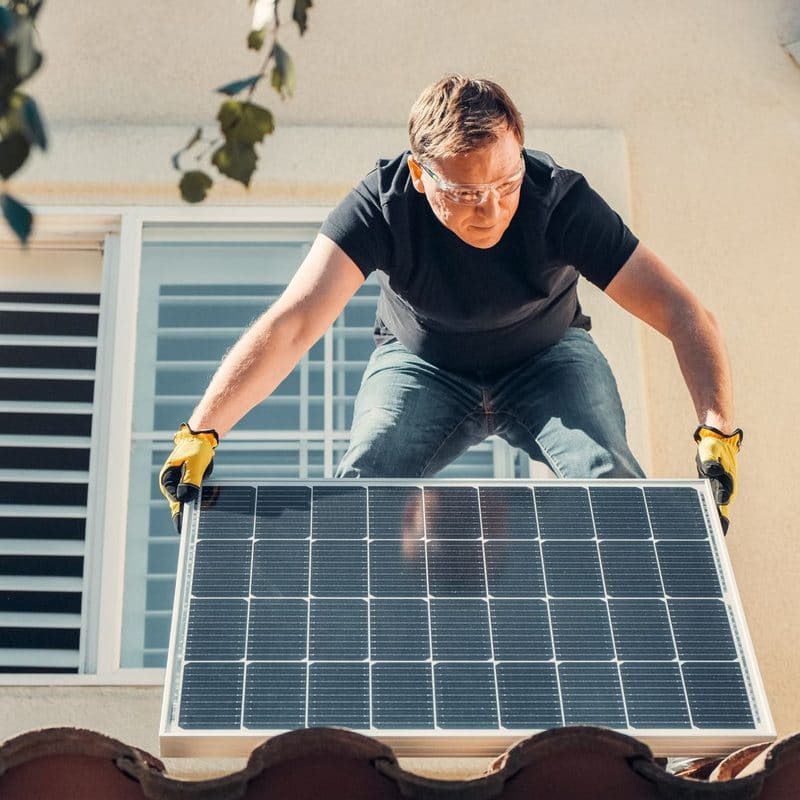 An installer lifting a solar panel onto a tiled roof