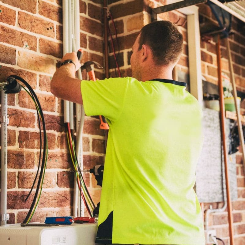 An electrician in a hi-vis shirt running cables on a brick wall