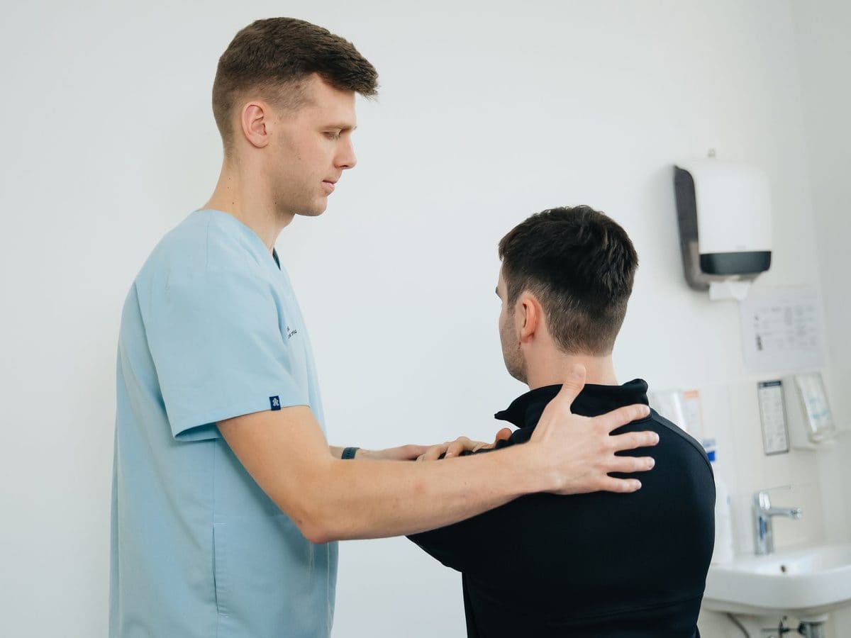 A physiotherapist checking a man's shoulder in a bright treatment room