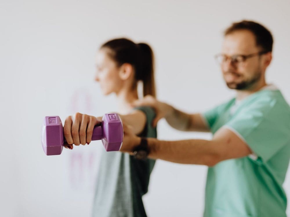An exercise physiologist steadying a woman's arm as she lifts a dumbbell