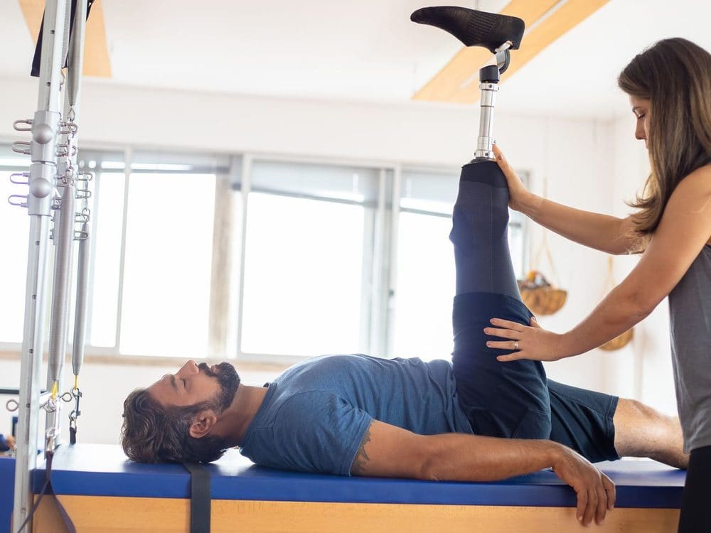 A practitioner guiding a man's leg on a clinical pilates reformer