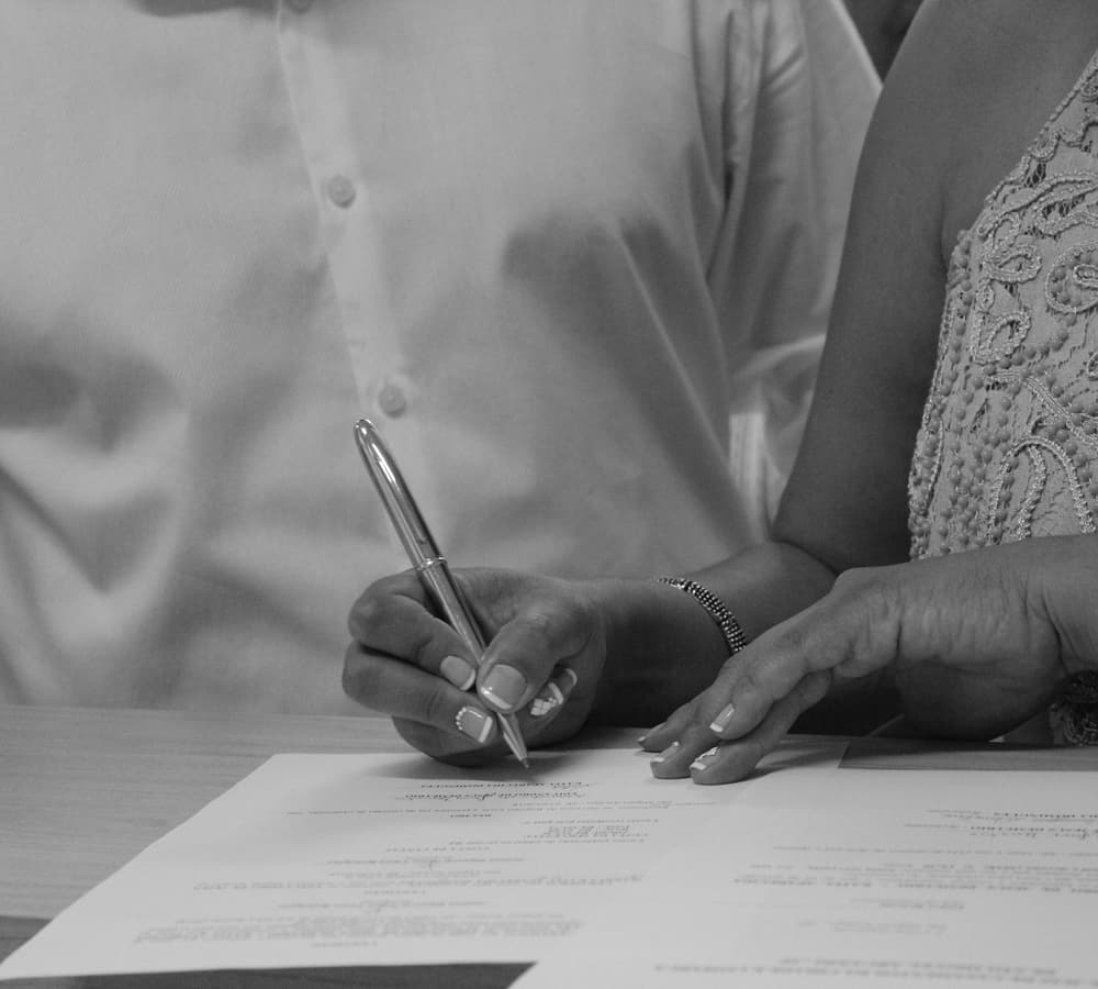 A person signing papers with a pen, in black and white