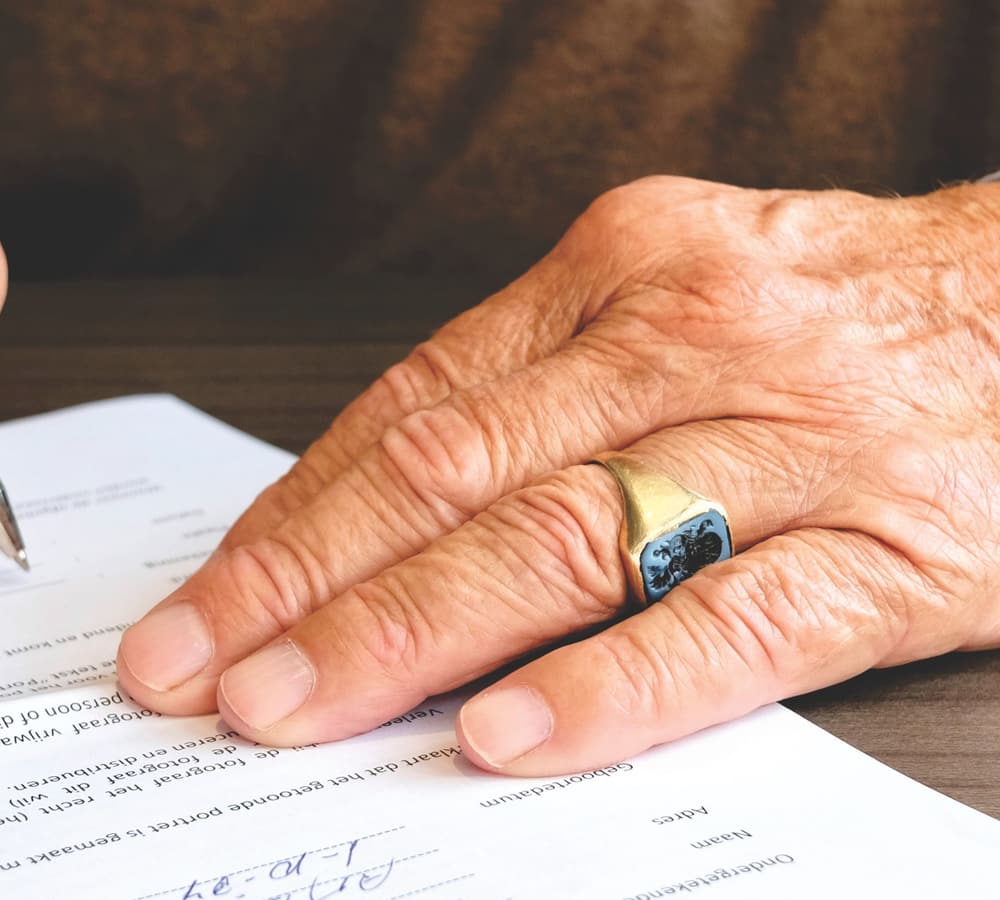 A hand with a wedding ring resting on a document beside a pen