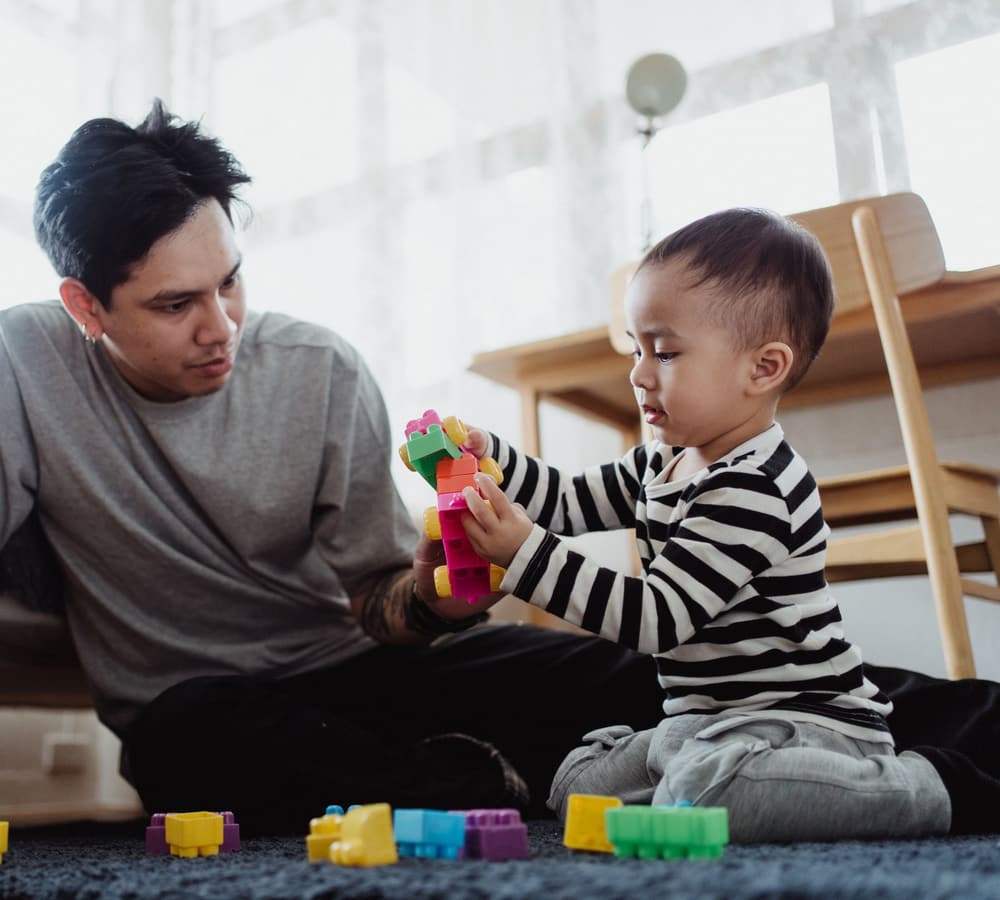 A father sitting on the floor playing with blocks with his young son
