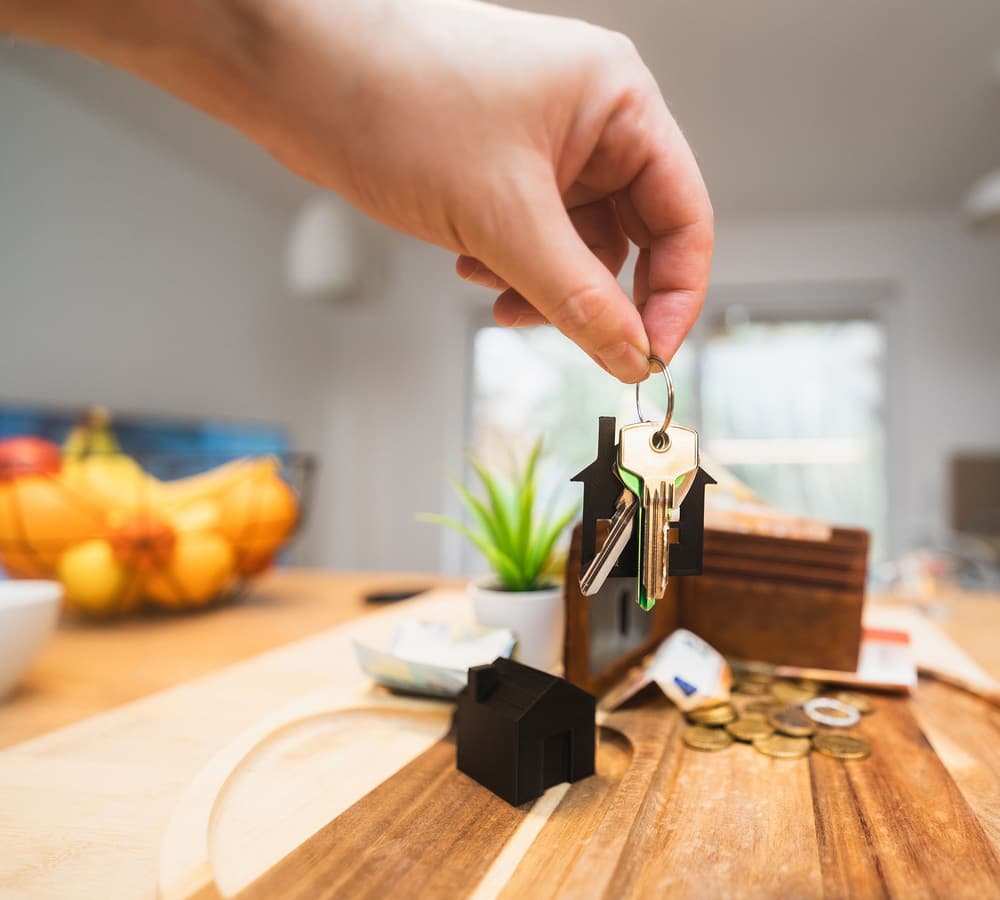 A hand holding house keys over a kitchen bench
