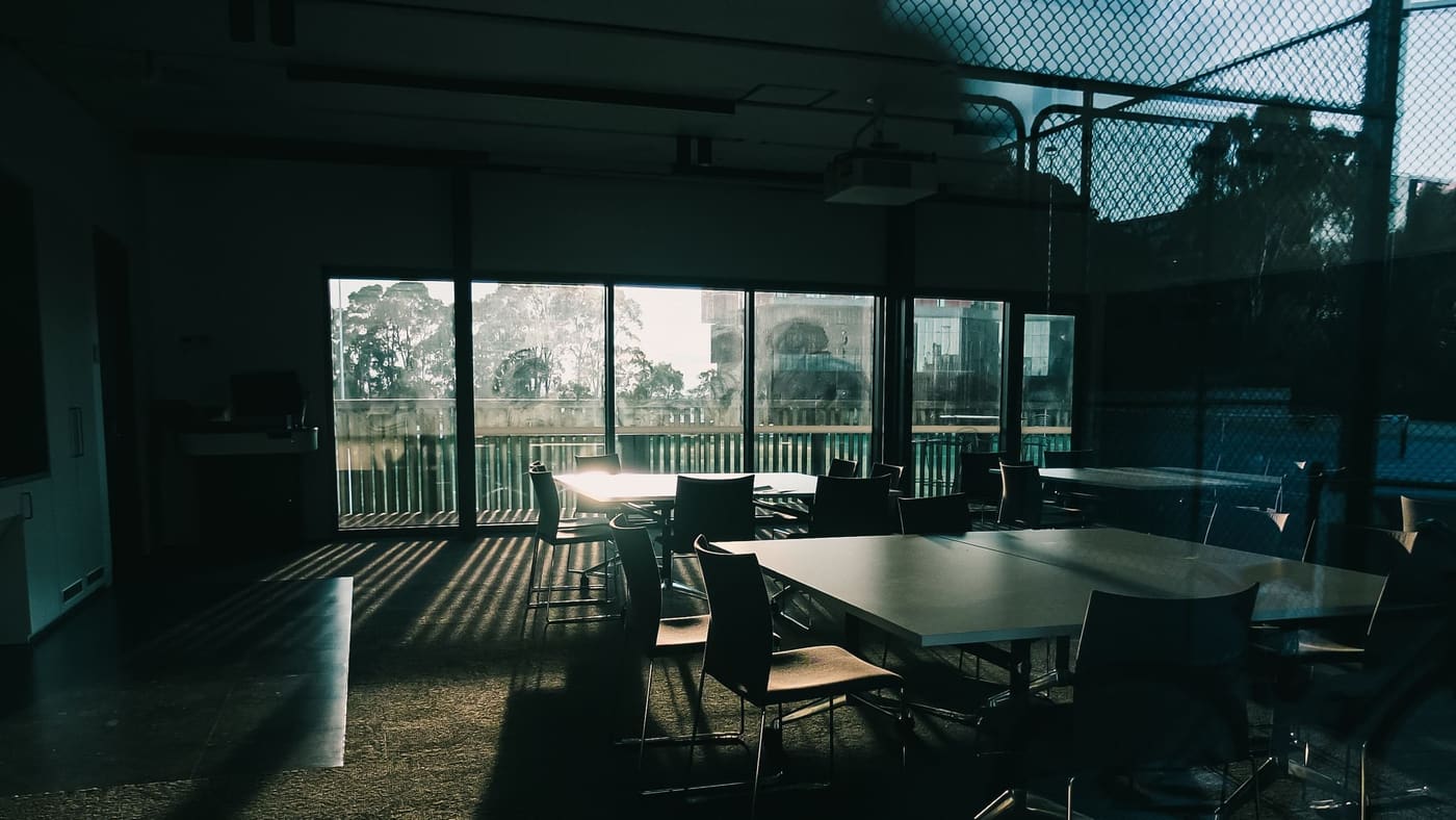 An empty meeting room with a long table and tall windows, in low light